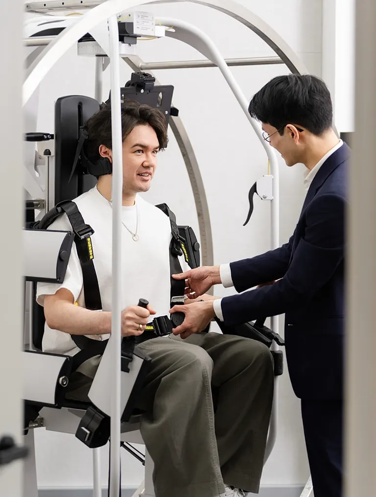 A patient seated and harnessed in the Rotundum positioning chair while a clinician talks them through the test